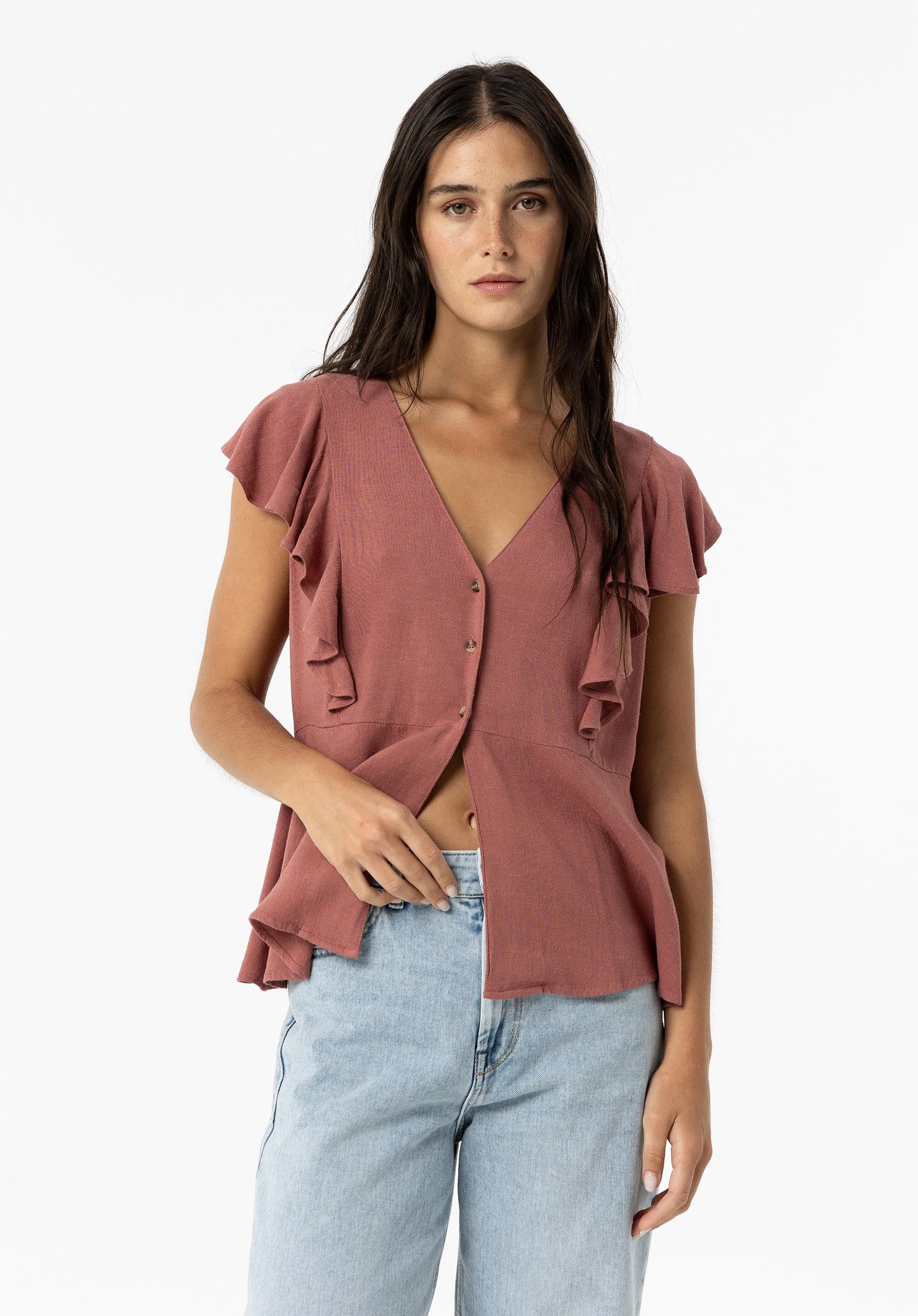 En kvinna poserar i en avslappnad outfit med en ljus volangblus och jeansshorts från Tiffosi